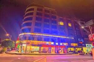 Un hotel de varios pisos con fachada curva, señalización iluminada y varios locales comerciales a nivel de calle.