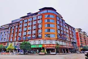 Un hotel de varios pisos con fachada curva, múltiples balcones y una zona comercial en la planta baja con tiendas.