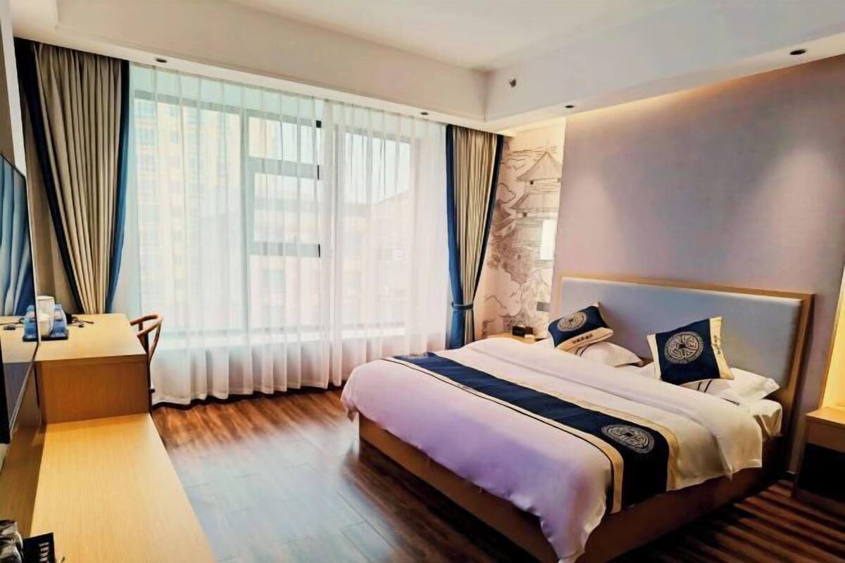 Una habitación de hotel con cama, escritorio y un ventanal con cortinas.