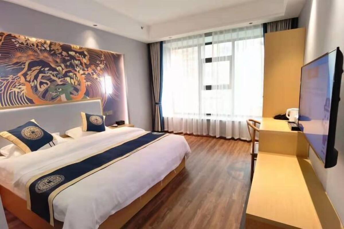 Habitación de hotel con cama, escritorio, silla, televisor y un cuadro grande en la pared.