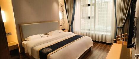 A hotel room with a large bed, a wooden floor, a bedside table, a TV, and a window with curtains.