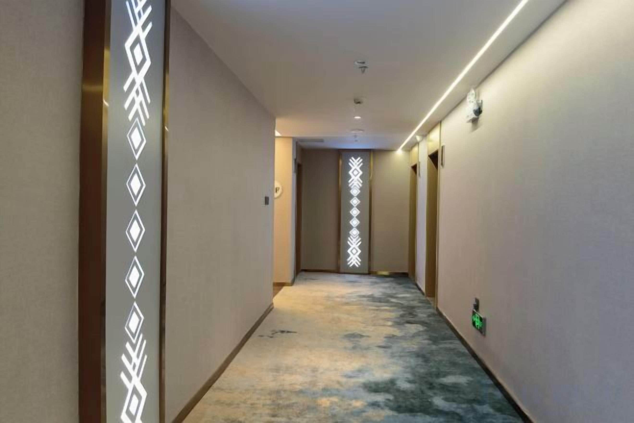 A hotel hallway with a carpeted floor, a light fixture on the ceiling, and a door at the end.