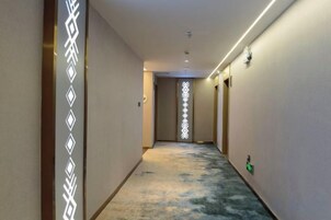 Un pasillo de hotel con piso alfombrado, una lámpara en el techo y una puerta al final.