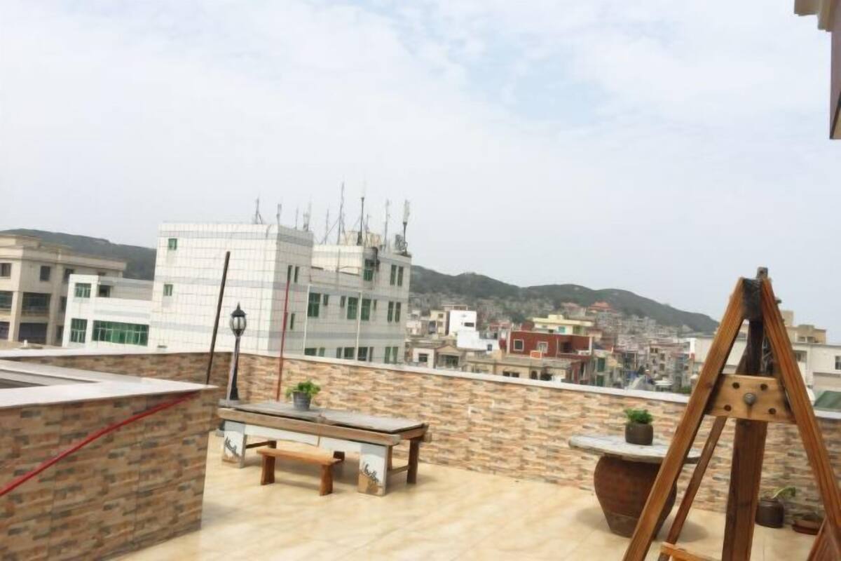 A rooftop terrace with a wooden bench, a table, and a wooden easel.
