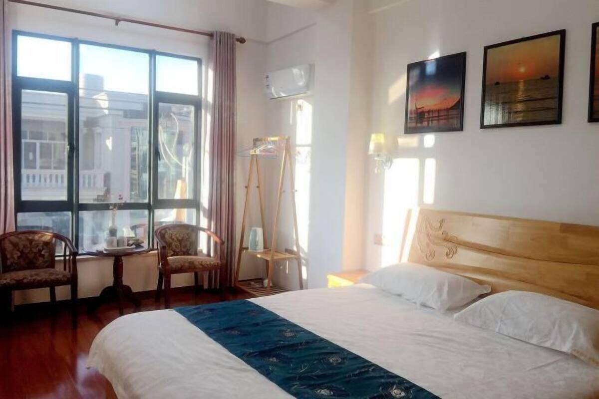 A hotel room with a large bed, two chairs, a small table, and a window with curtains.