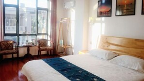 Une chambre d’hôtel avec un grand lit, une tête de lit en bois, une fenêtre avec des rideaux, une petite table avec des chaises et des œuvres d’art accrochées au mur.