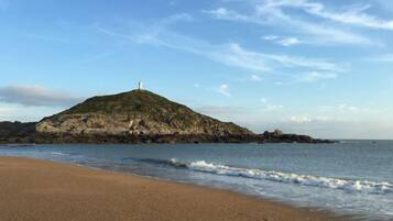 A beach with a rocky island and a lighthouse in the distance.