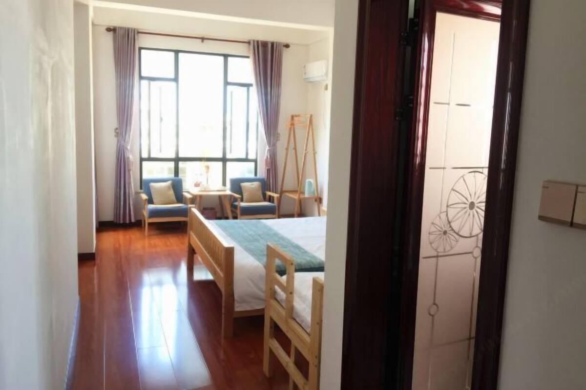 A room with a bed, a desk, two chairs, a window with curtains, and a wooden floor.