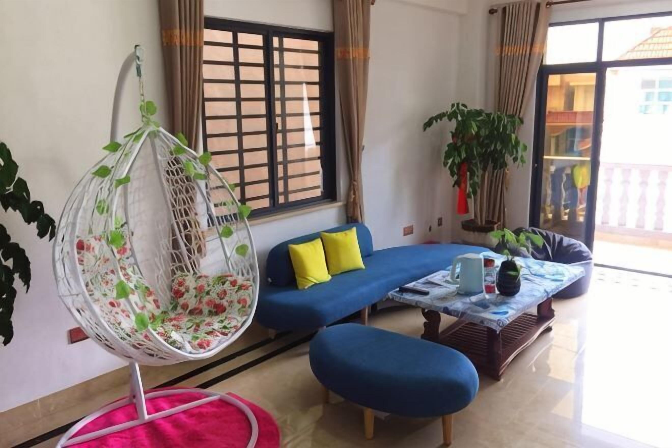 A living room with a hanging chair, a blue sofa, a coffee table, and a window with curtains.
