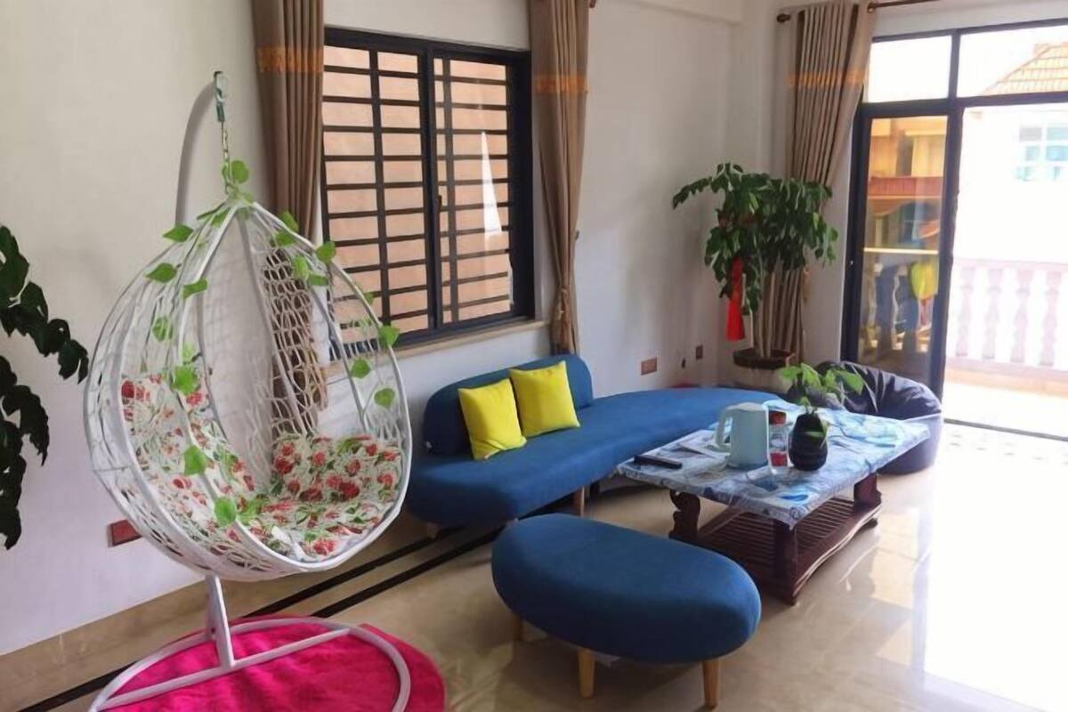 A living room with a hanging chair, a blue sofa, a coffee table, and a window with curtains.