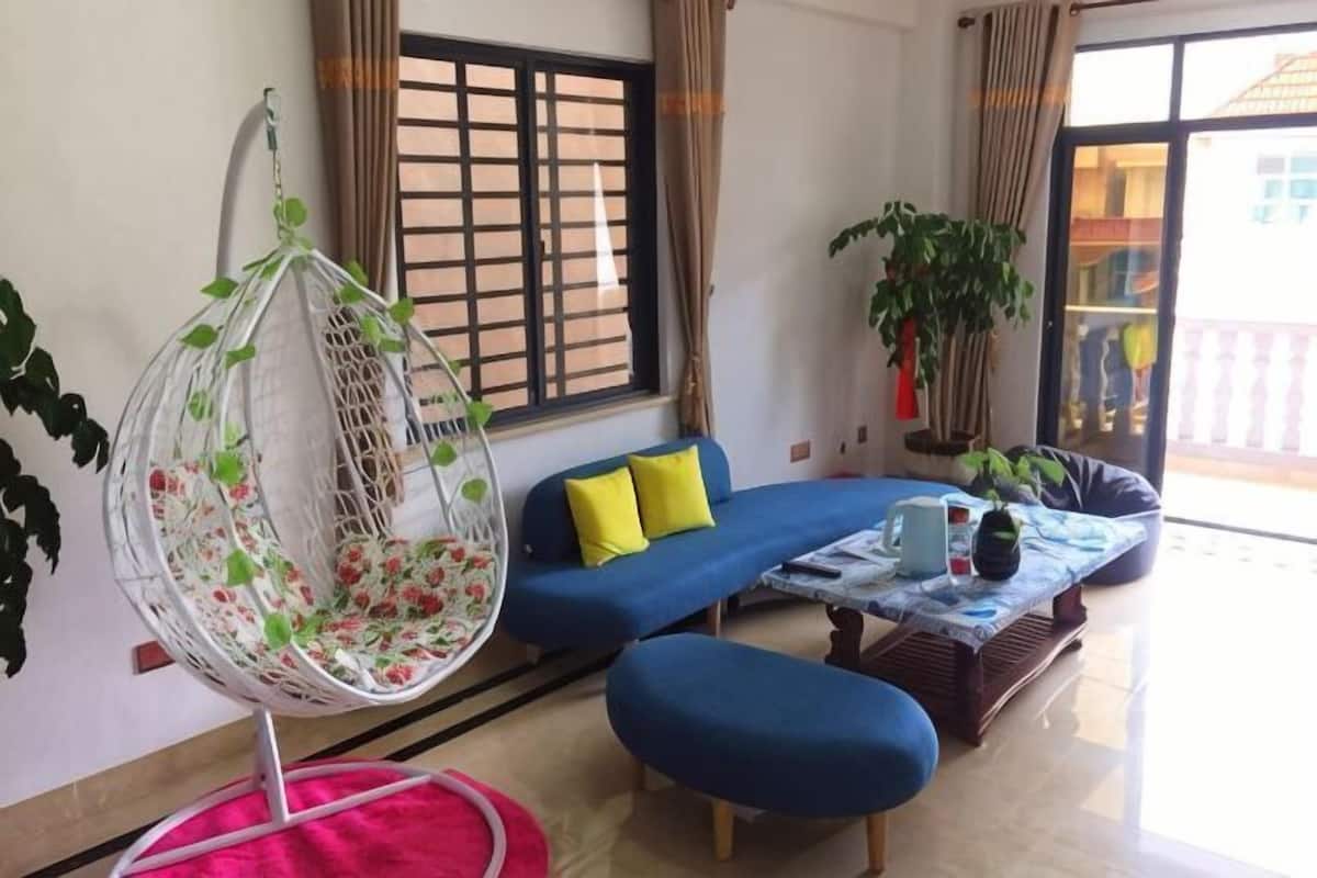 A living room with a hanging chair, a blue sofa, a coffee table, and a window with curtains.