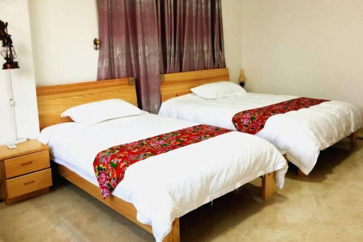 Two single beds with wooden frames and white bedding, a wooden nightstand with drawers, and a curtain on the window.