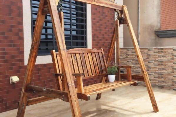 Un portique en bois se trouve devant un bâtiment en briques, avec une fenêtre et un pot de fleurs.