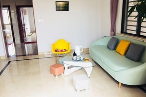 Un salon moderne avec un canapé vert, un fauteuil jaune, une table basse en verre et un petit pouf blanc.