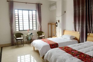 Quarto de hotel com duas camas, uma mesinha com cadeiras, uma luminária e uma janela com cortinas.