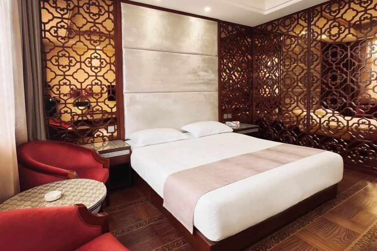 A hotel room with a bed, a red chair, a small table, and decorative wooden panels.
