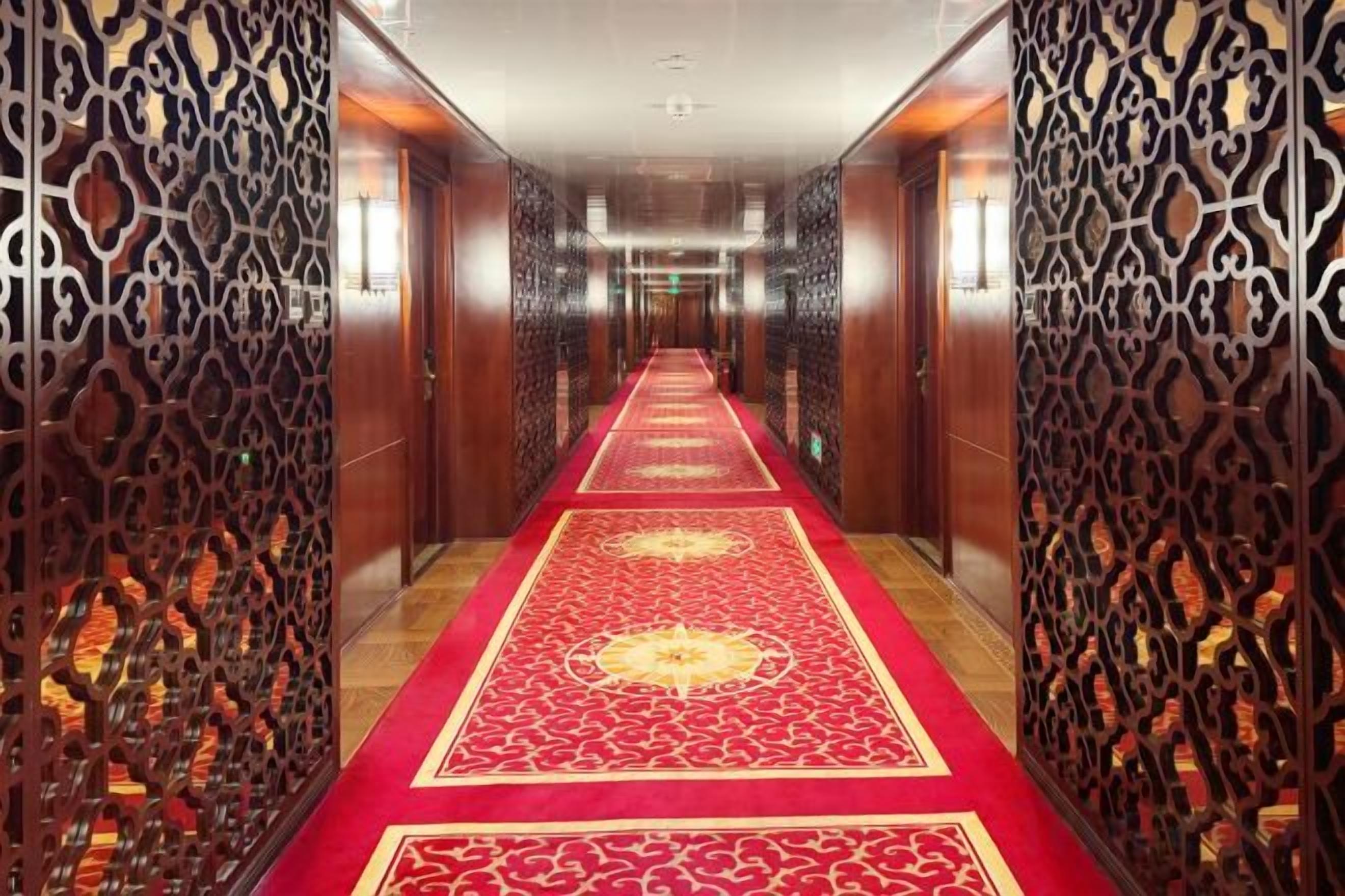 A hallway with a red carpet, wooden paneling, and a patterned design.