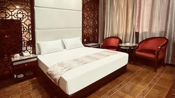 Ein Hotelzimmer mit einem großen Bett, zwei roten Sesseln, einem kleinen Tisch, einem Nachttisch und einem Vorhang mit Muster.