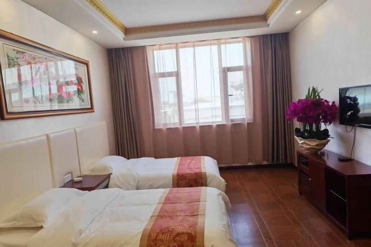 A hotel room with two beds, a television, a desk, a window with curtains, and a painting on the wall.