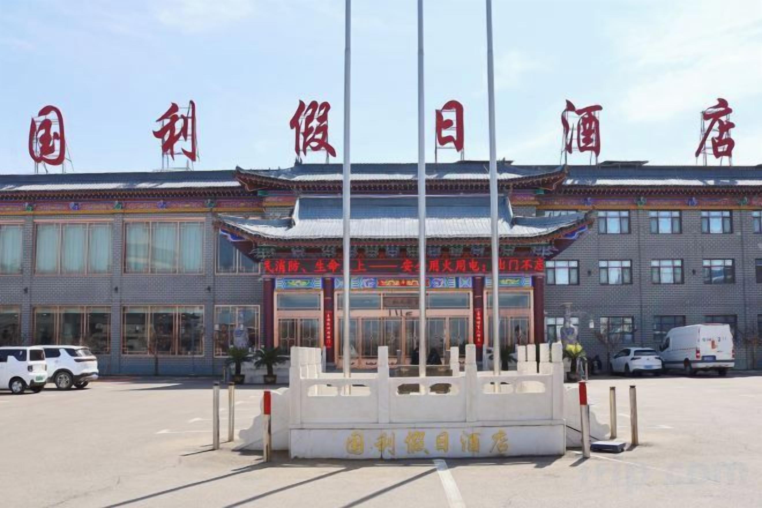 A traditional building with a sign in a foreign language, a flagpole, and a parking lot.