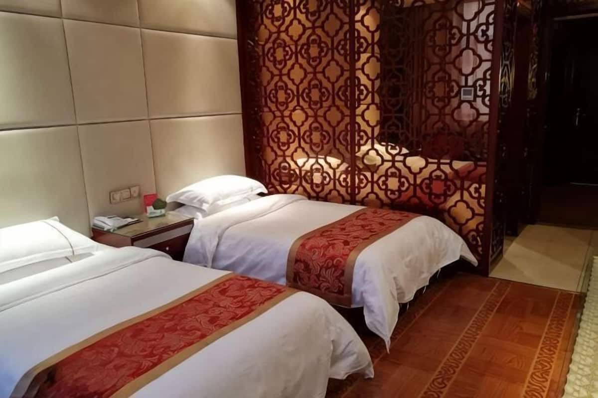 A hotel room with two beds, a headboard, a nightstand, and a patterned curtain.