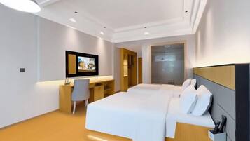 A modern hotel room with a large bed, a desk with a chair, a TV, and a wardrobe.
