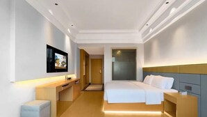 A modern hotel room with a bed, bedside table, TV, and a small seating area.