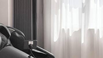 A modern room with a bed, a bedside table, and a window with sheer curtains.
