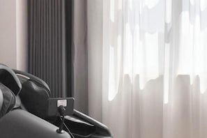 Una habitación moderna con una cama, una mesita de noche y un ventanal con cortinas traslúcidas.
