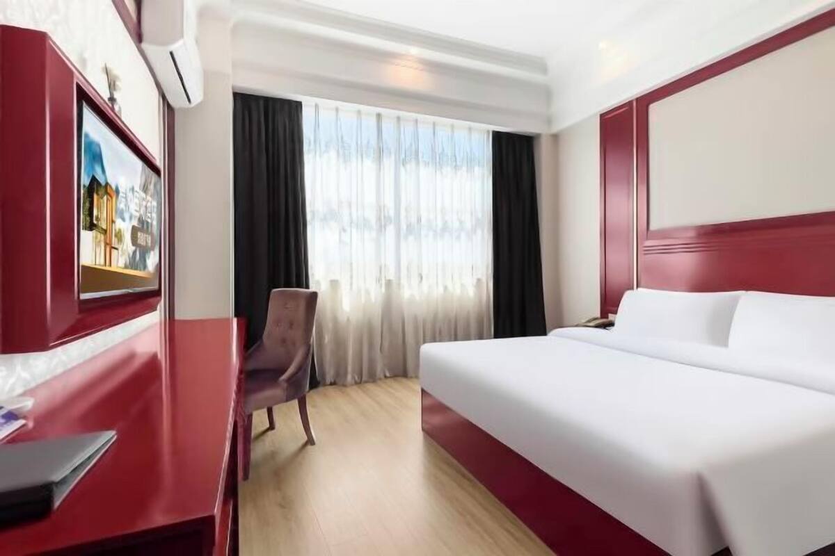 Quarto de hotel com cama, escrivaninha, cadeira e janela com cortinas.