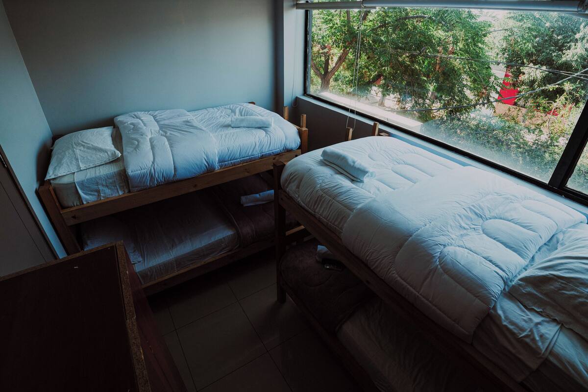 Une chambre de dortoir avec deux lits superposés, une fenêtre donnant sur des arbres et un bureau en bois.