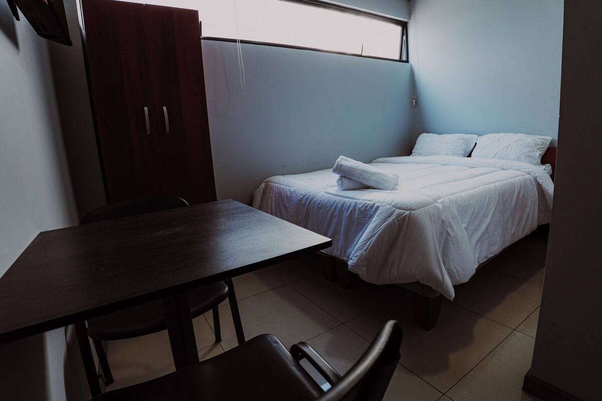 Une petite pièce, bien rangée, avec un lit, une table et une chaise.