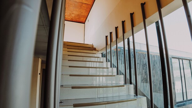 Una escalera moderna con barandillas de vidrio y acabado de madera, que conduce a un nivel superior.
