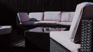 Un espacio de estar al aire libre con muebles de mimbre, cojines y una mesa de vidrio.