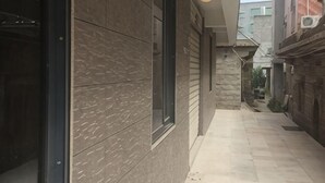 Un couloir étroit avec la façade d’un immeuble moderne, une fenêtre visible et une porte sur la gauche.