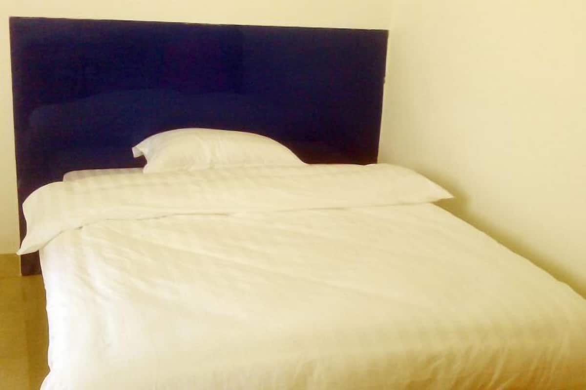 Ein Bett mit dunkelbrauner Kopfteil, weißer Bettwäsche und einer schlichten Wand.