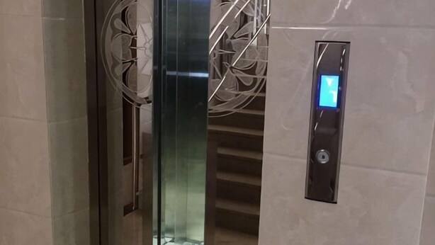 Un ascenseur moderne doté d’un écran numérique, d’une porte en verre et d’une main courante métallique.