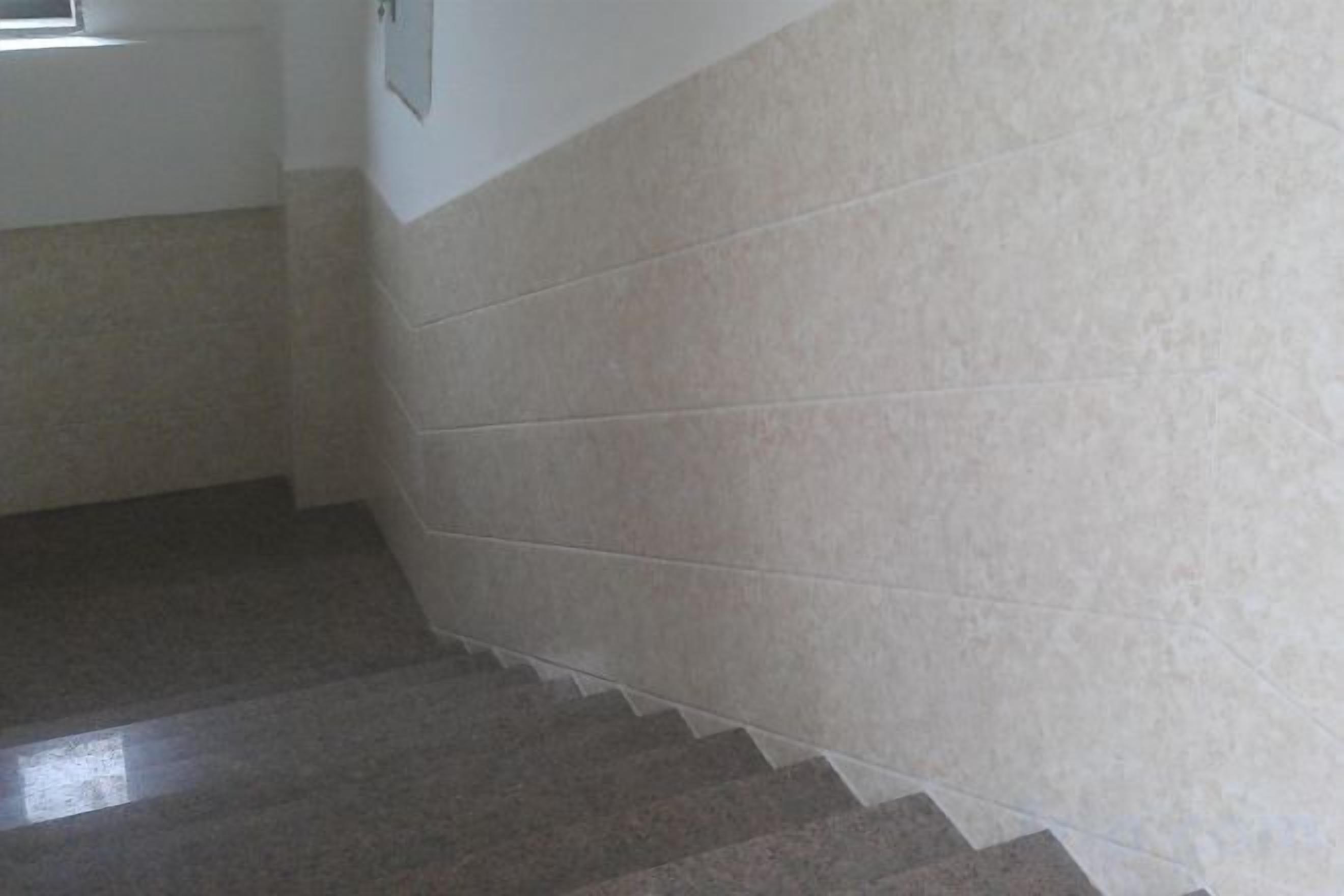 Een trap met een lichtgekleurde muur en een donkere vloer.