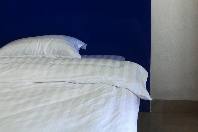 A bed with white bedding in a room with a blue wall and a white door.