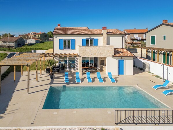 A two-story house with a swimming pool, outdoor seating, and a pergola.