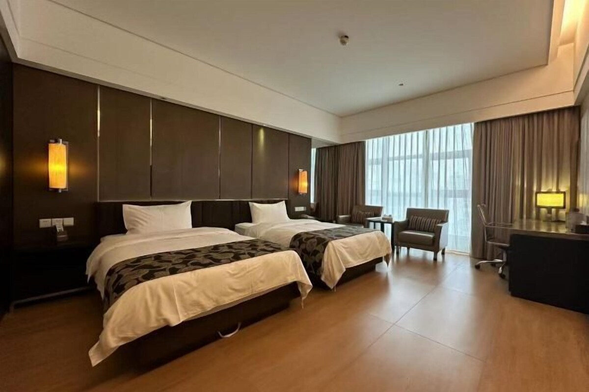 Een hotelkamer met twee bedden, een bureau, een stoel en een groot raam.