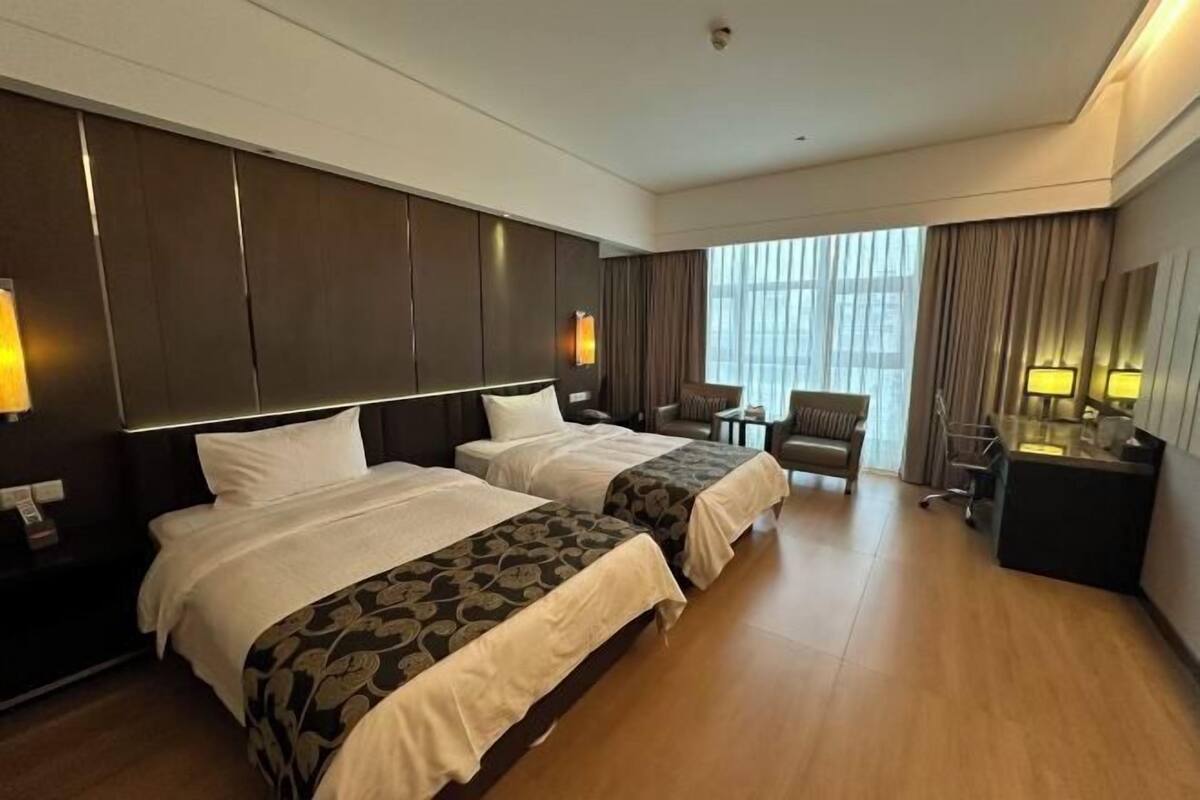 Habitación de hotel con dos camas, un escritorio, una silla y un ventanal grande.