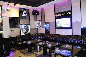 A lounge area with a curved black leather sofa, a flat-screen TV, and a Louis Vuitton sign. - Huasheng Shaxian Boutique Hotel (Sanming)