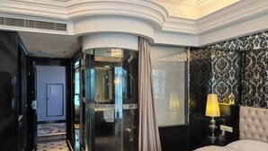 A hotel room with a curved glass partition, a bed with a patterned bedspread, a nightstand with a lamp, and a wall with a decorative pattern. - Huasheng Shaxian Boutique Hotel (Sanming)