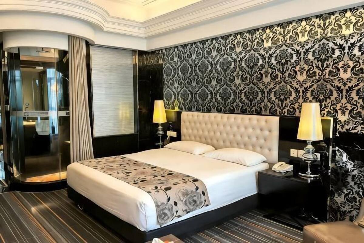 Habitación de hotel con una cama grande, baño independiente, papel tapiz estampado y una mesita de noche con lámpara.