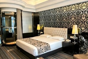 Ein Hotelzimmer mit einem großen Bett, einem separaten Badezimmer, einem gemusterten Wandteppich und einem Nachttisch mit einer Lampe.