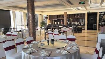 A banquet hall with round tables set for dining, a large pillar, and a bar area in the background.