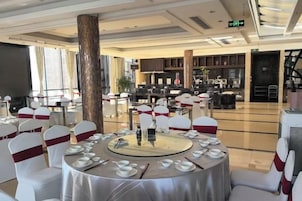 Un salón de banquetes con mesas redondas dispuestas para cenar, un pilar grande y una zona de bar al fondo.