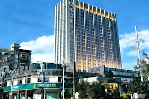 Um hotel alto com fachada moderna, área comercial no térreo e um céu azul límpido.