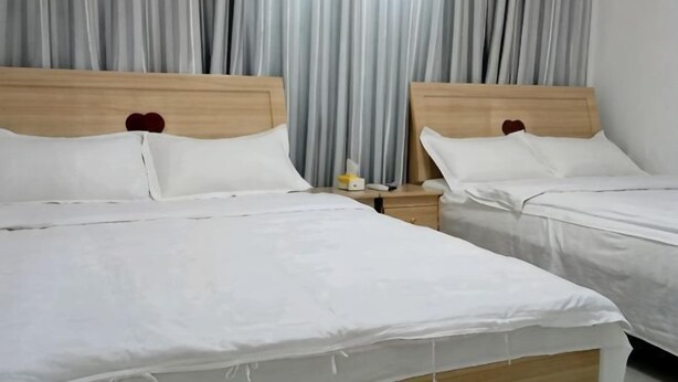 A hotel room with two beds, a wooden headboard, white bedding, a nightstand with a phone and a bottle, and a window with curtains.